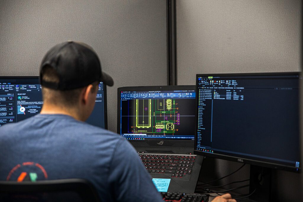A man at an industrial desk with two monitors in front of him, working on power services.